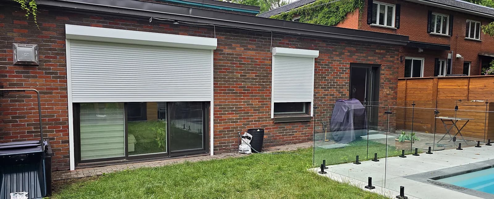White roller shutters on a brick house with a pool, Montreal